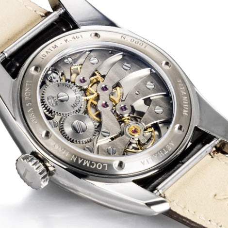 Close-up of a LOCMAN wristwatch back showing a detailed OISA automatic mechanical movement with silver-toned gears and a beige leather strap on a white background.