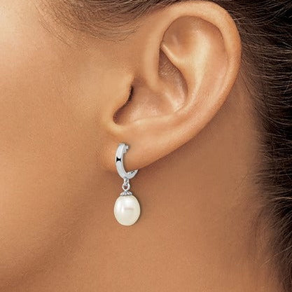 A close-up of a model's ear wearing a silver huggie hoop earring with a dangling white pearl.