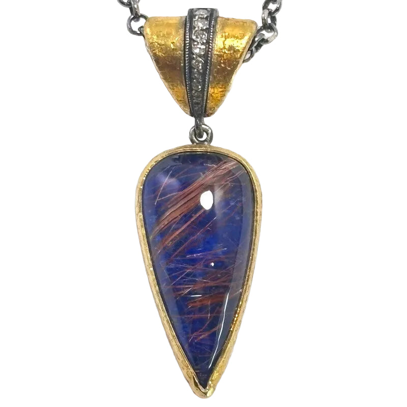 A teardrop-shaped pendant necklace featuring a blue glass cabochon with coppery metallic linear inclusions, set in a gold and silver-tone metal frame with a textured gold bail.