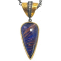 A teardrop-shaped pendant necklace featuring a blue glass cabochon with coppery metallic linear inclusions, set in a gold and silver-tone metal frame with a textured gold bail.