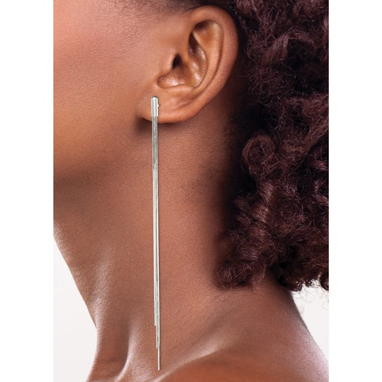 A close-up of a model's ear and neck wearing a long, thin silver dangle earring with a textured metallic finish.